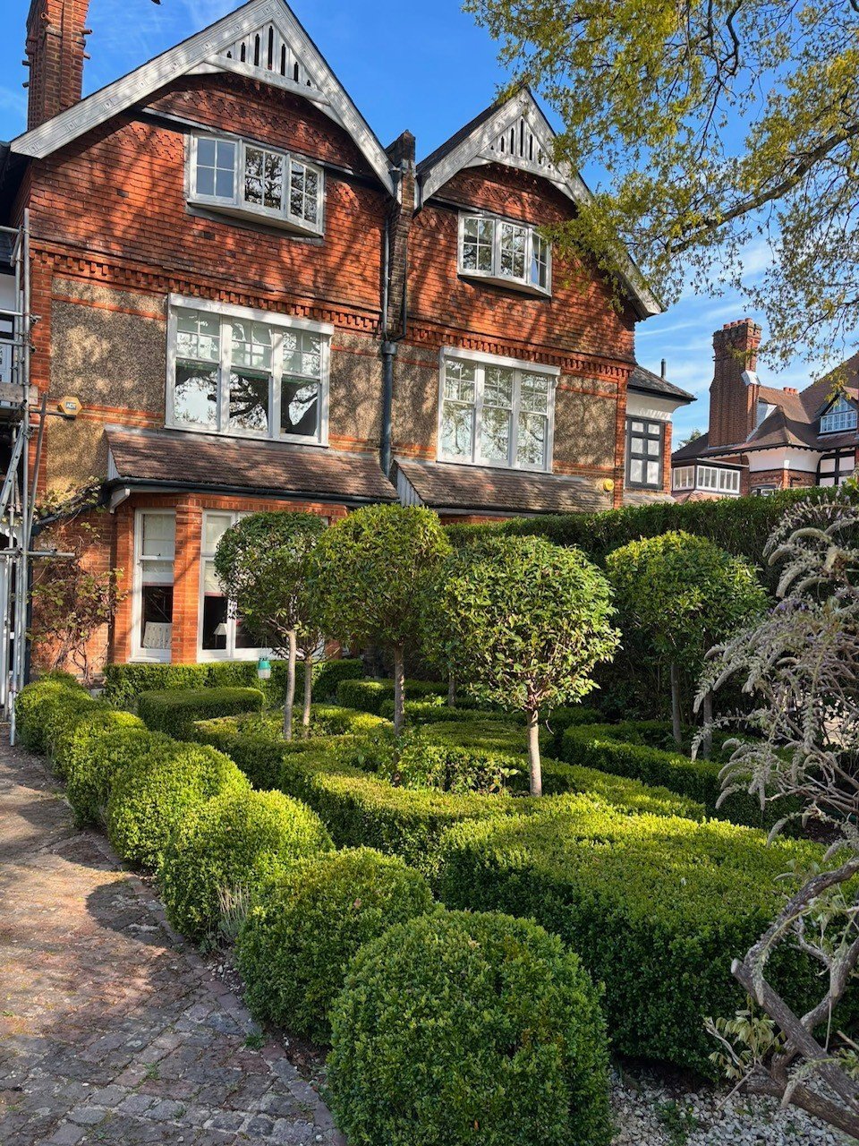 Victorian brick house with manicured topiary hedges in the front garden under a clear blue sky